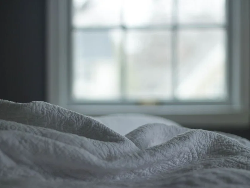 Chambre sobre, couette claire près d’une fenêtre dans la lumière douce d’un matin d’hiver